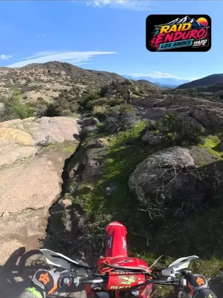 Sendero de piedra suelta que sube por la ladera, con la cordillera nevada al fondo.